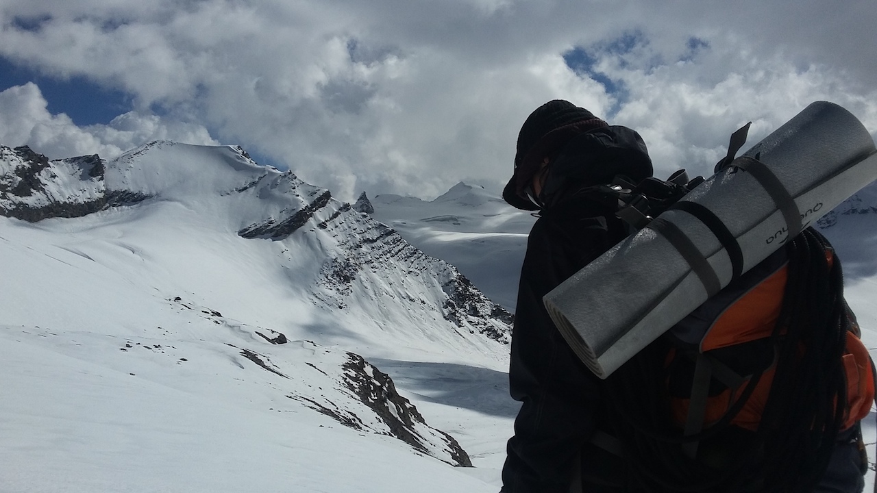 Trekker walking over snow capped mountain under cloudy sky