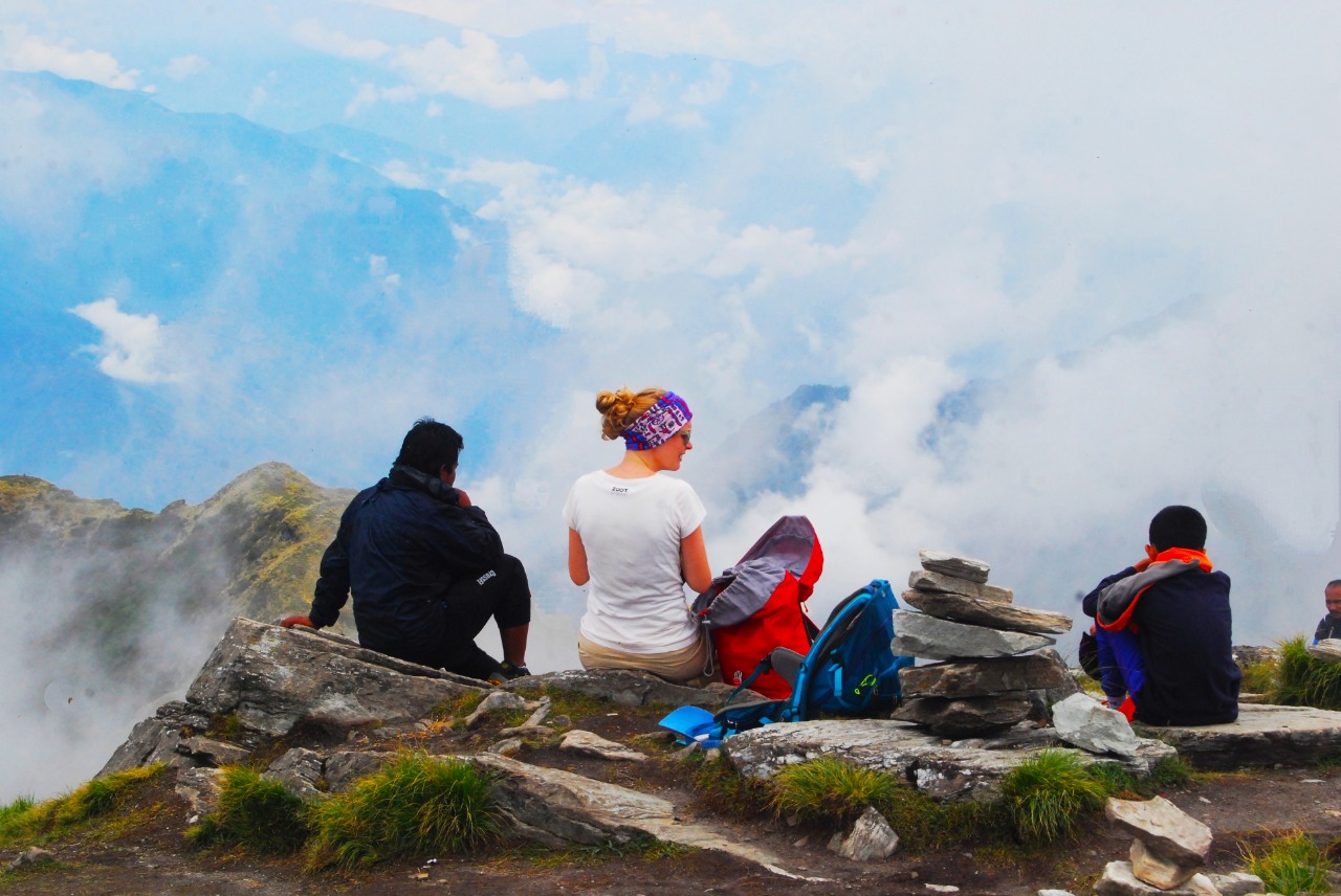 Trekkers resting at the chandrashila peak with stone placed on one another at right, glancing at the beautiful view of mist covering the   valley