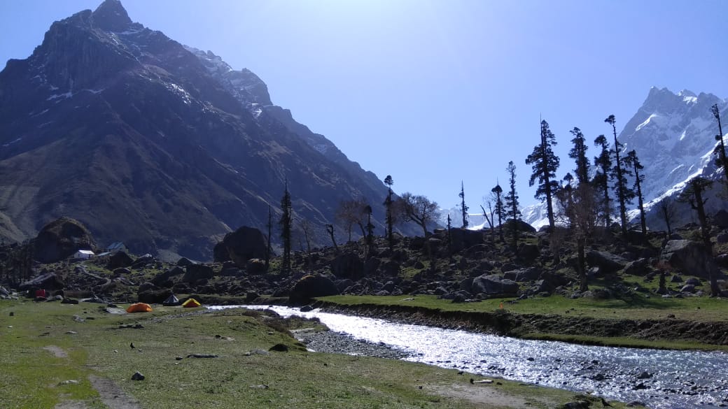 Tents pitched on one side of river and beautiful mountains the= other covered with snow