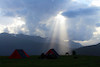 couple of tents pitched at badni campsite with sun shattering its light through the little space in clouds