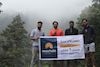 trekkers holding banner of roopkund trek with mist covereing the back of mountain